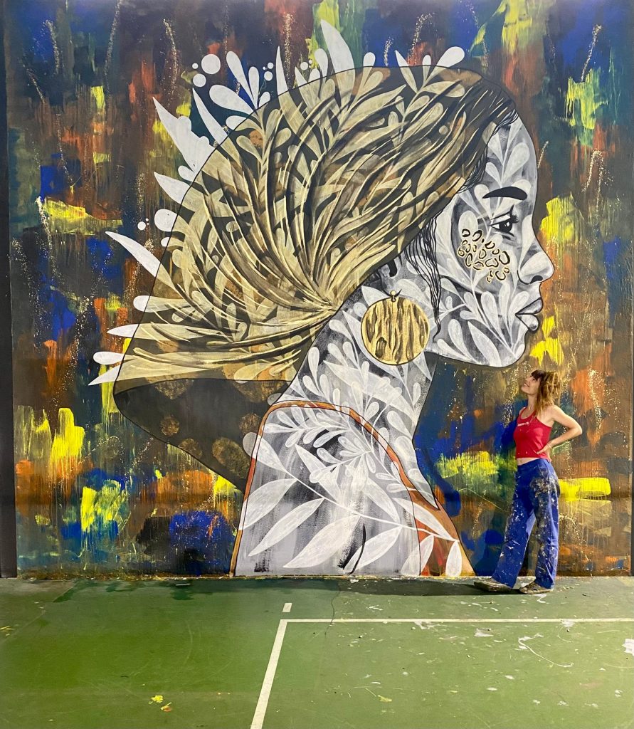 Tanala regarde son œuvre, un grand portrait aux plumes dorées, à la Halle des sports de Canohès