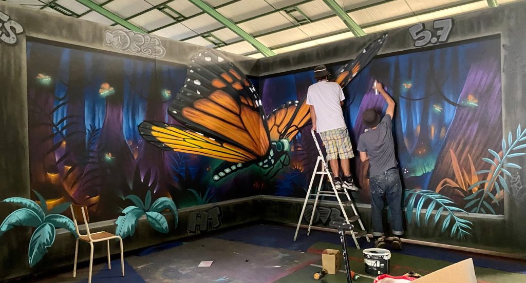Deux artistes peignent la fresque du papillon à la Halle des sports de Canohès